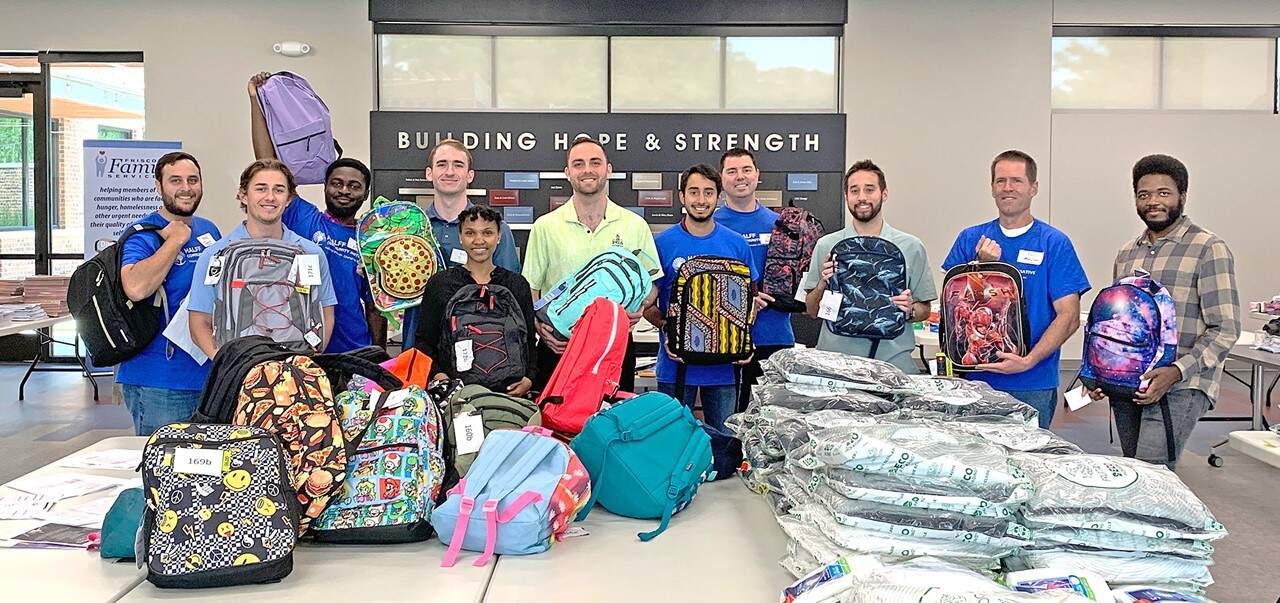 Halff Frisco volunteers holding backpacks at Frisco Family Services back-to-school drive