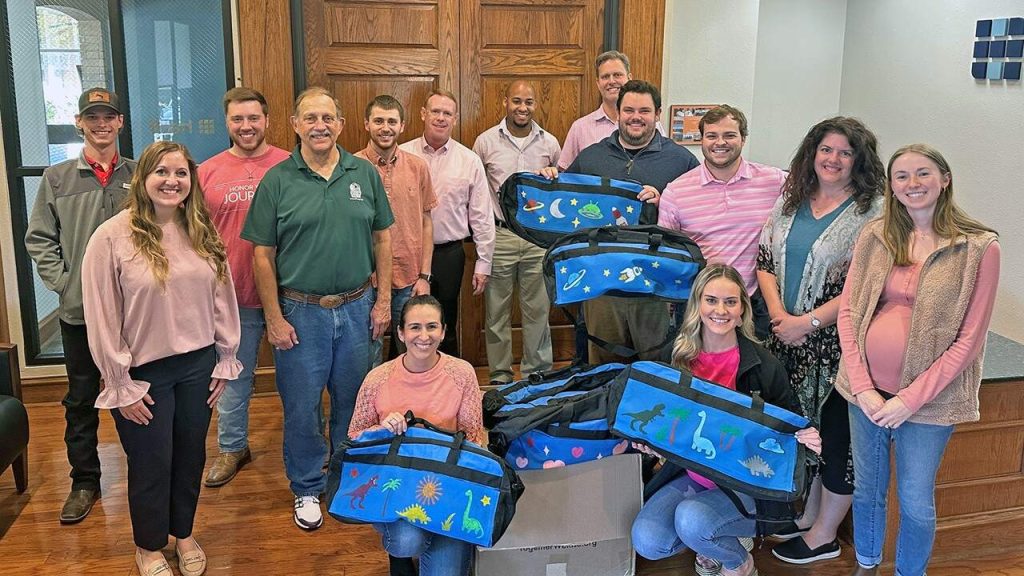Halff's Tyler office group holding up sweet cases duffle bags donations